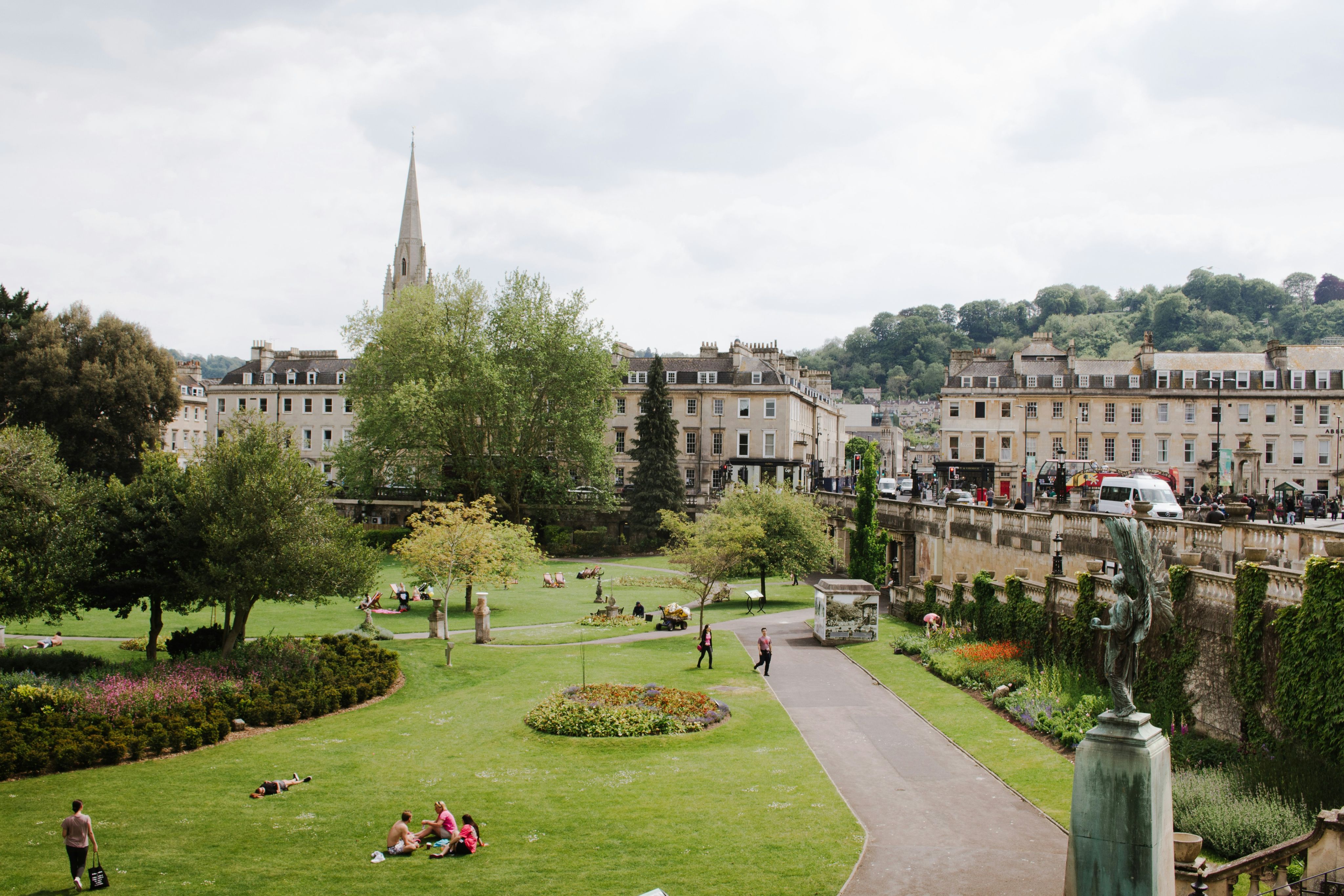 An image of Bath, England, showing its typical light Roman buildings and a green tree filled park
